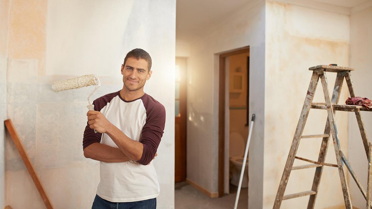 Man holding roller brush in a room half painted